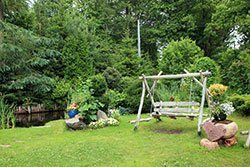A wooden swing is sitting in the middle of a lush green garden in Columbus