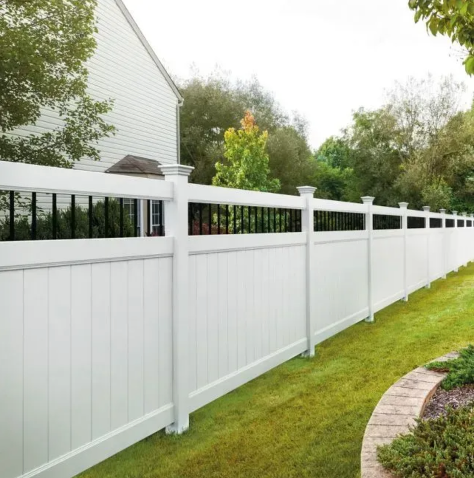 A white vinyl privacy fence with a decorative black metal top railing runs along a grassy yard next to a house in Columbus