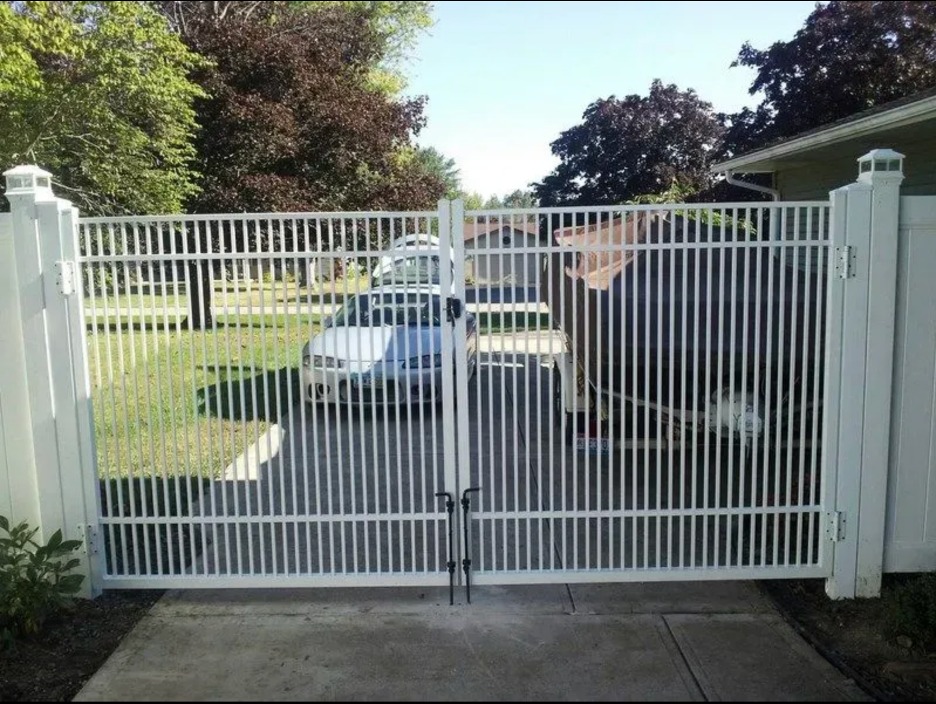 A white metal double-swing driveway gate set between two white posts on a suburban residential driveway in Columbus