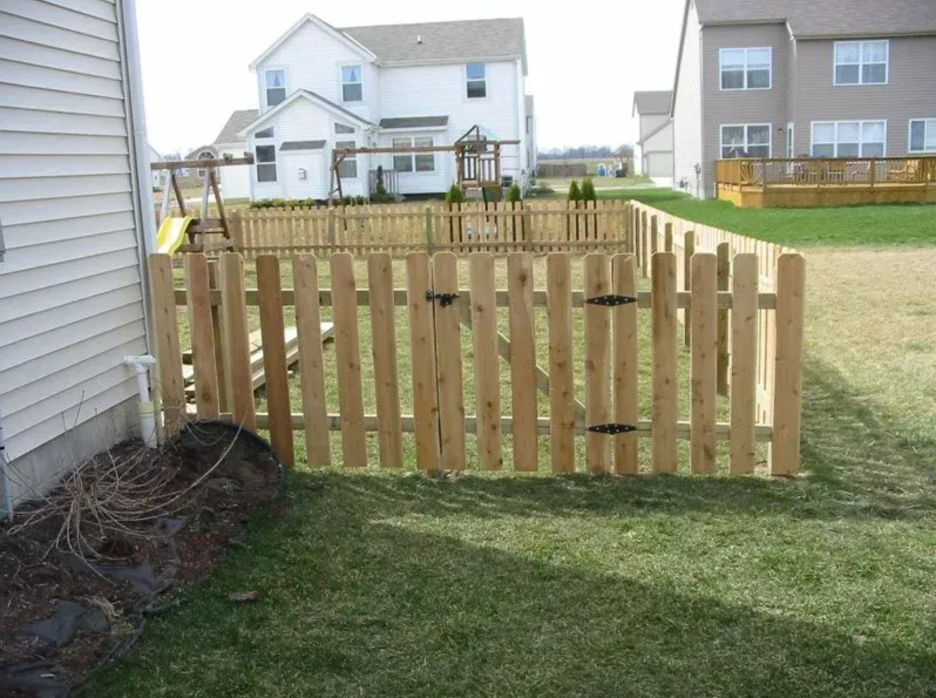 A new wooden picket fence enclosure sits on a suburban lawn next to a house, featuring a gated entrance in Columbus