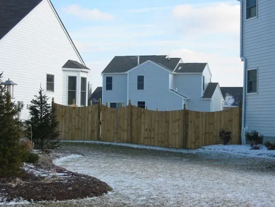 A curved wooden fence separates suburban houses on a lawn dusted with light snow in Columbus