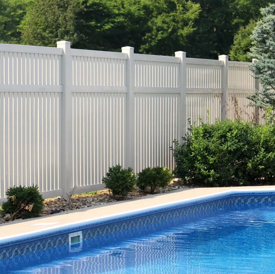 A bright blue swimming pool bordered by a white privacy fence and green landscaping in Columbus