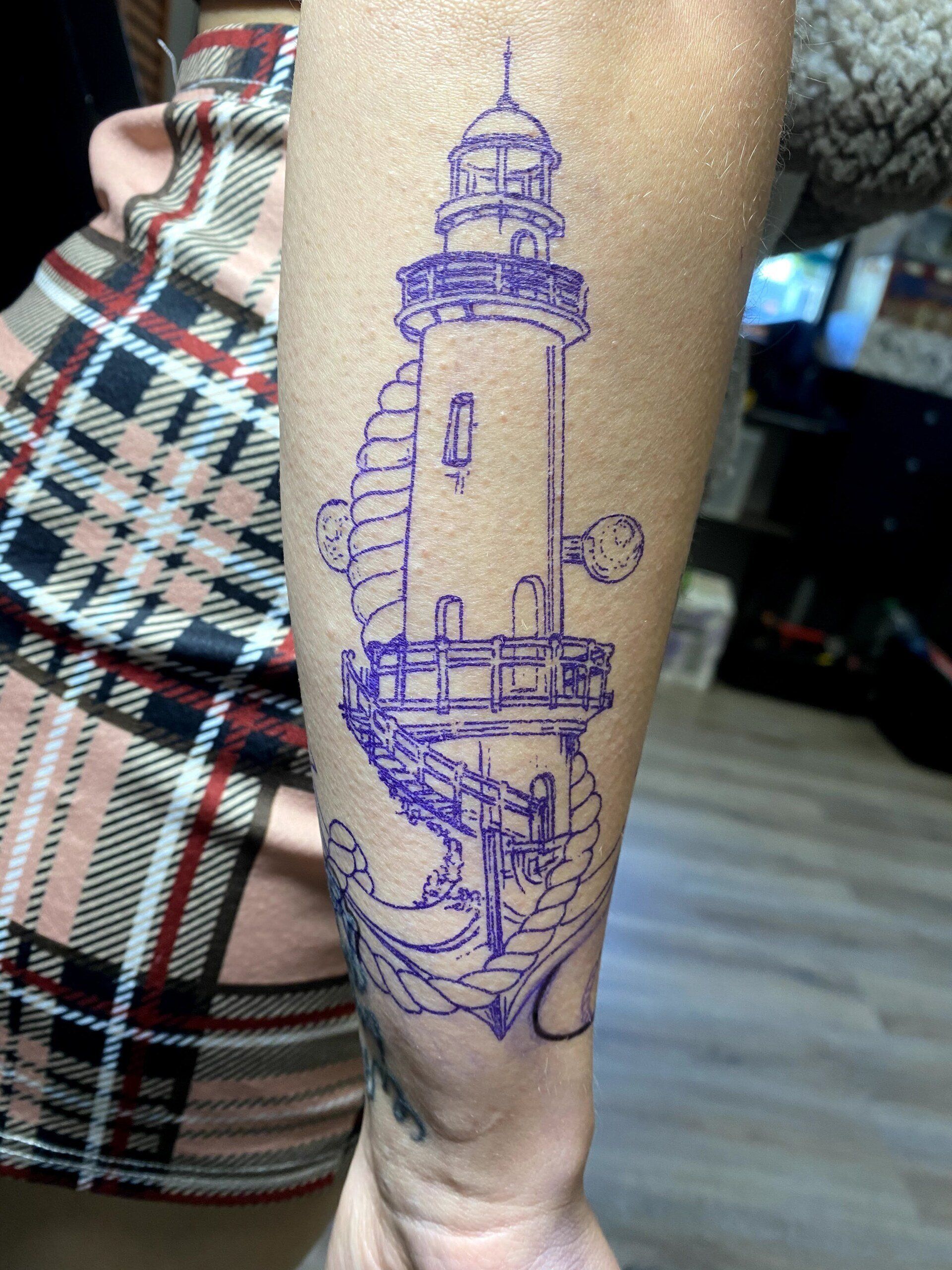 A woman has a tattoo of a lighthouse on her arm