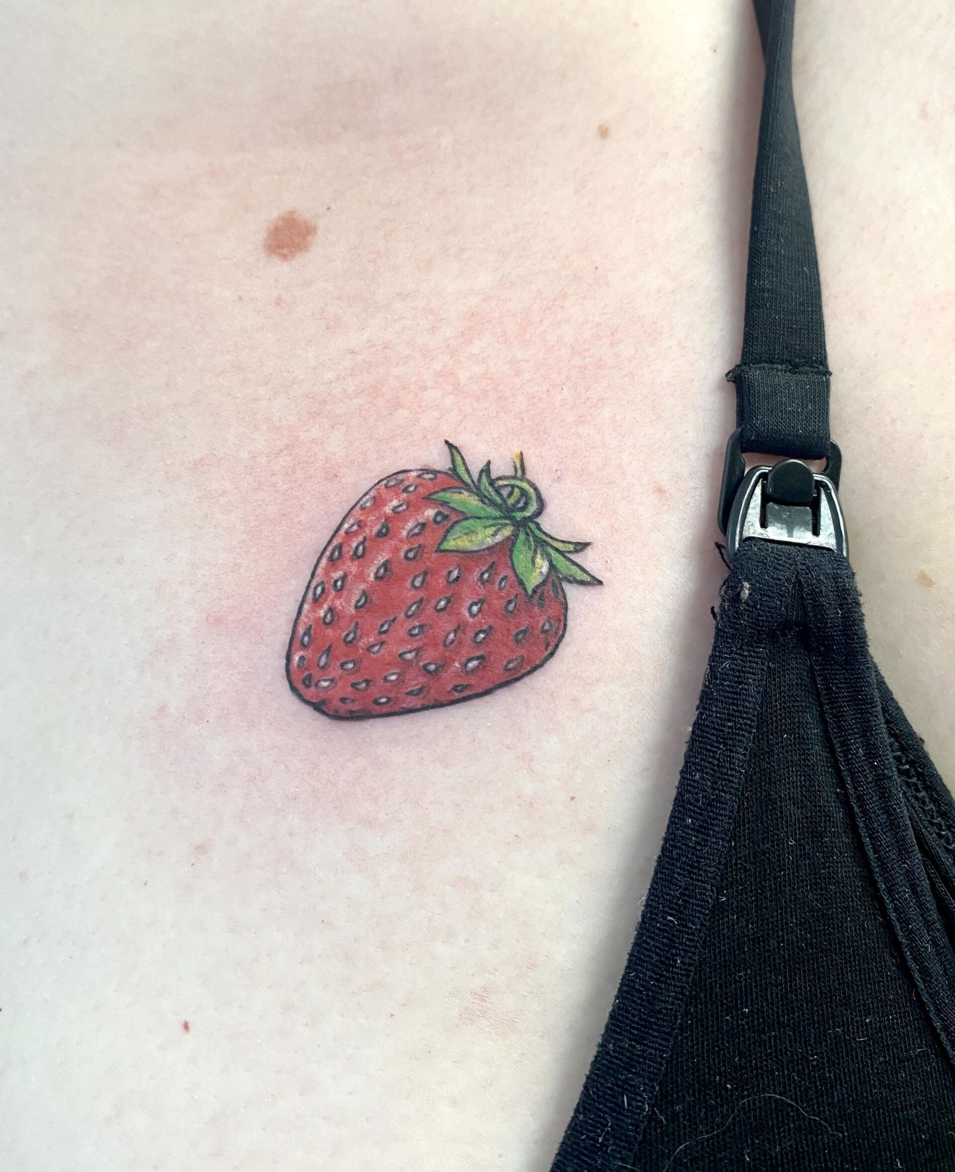 A woman has a small tattoo of a strawberry on her chest.
