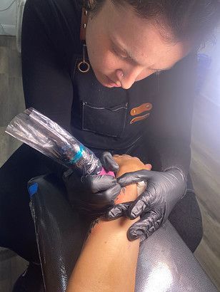 A woman is getting a tattoo on a person 's wrist.