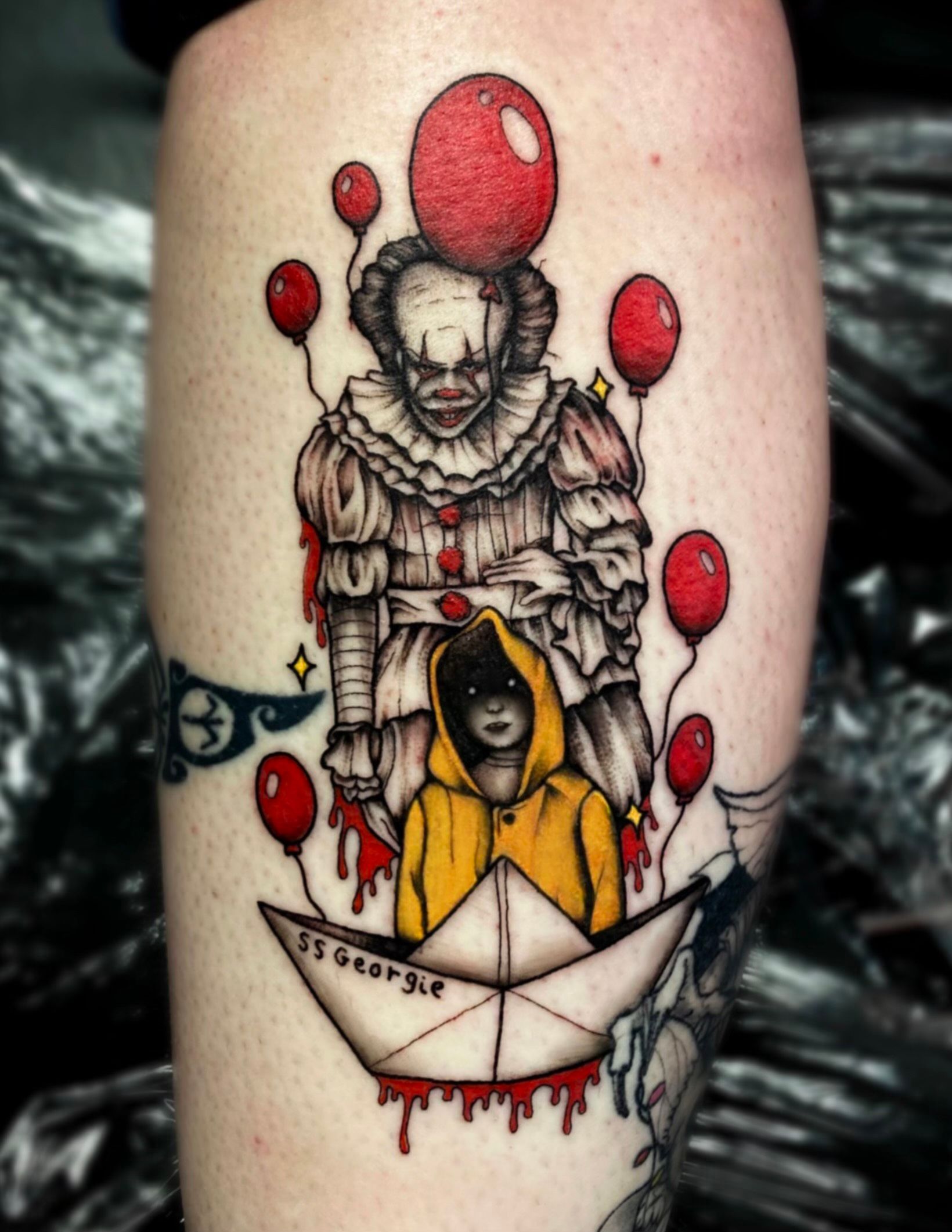 A tattoo of a clown and a child in an origami boat