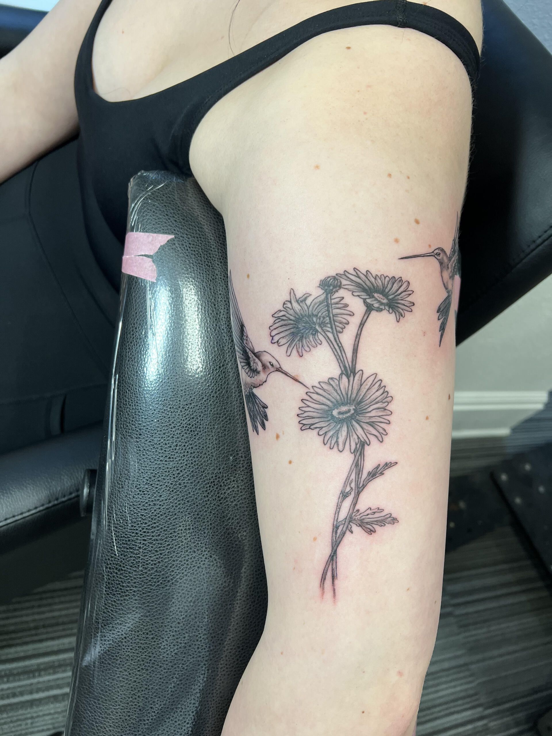 A woman has a tattoo of flowers and a hummingbird on her arm