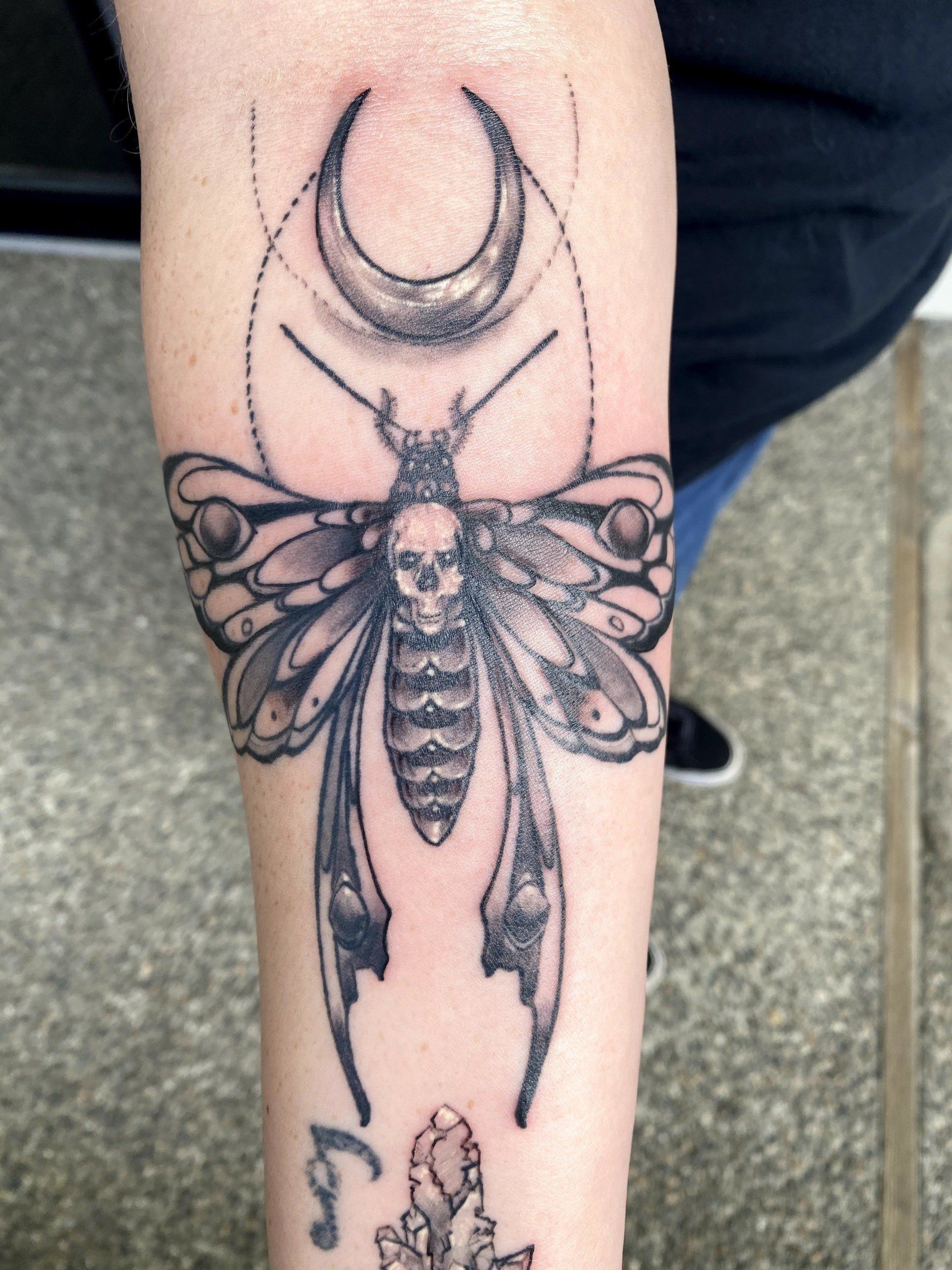 A tattoo of a moth with a skull and a crescent moon