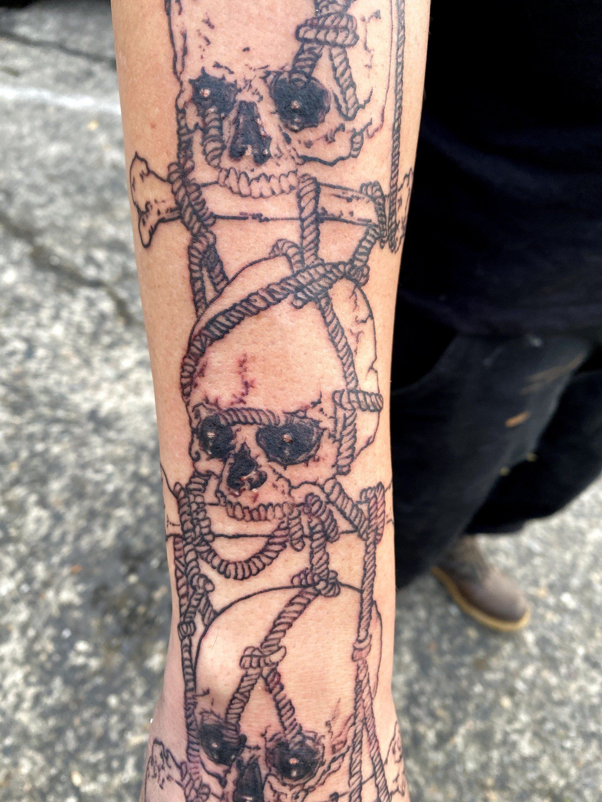 A person has a tattoo of skulls and ropes on their arm