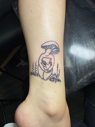 A woman is sitting under a mushroom tattoo on her ankle.
