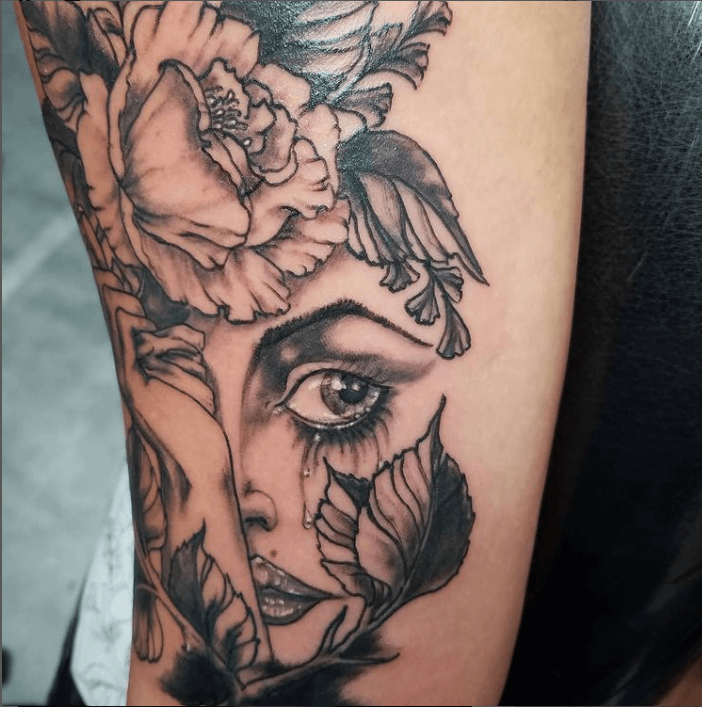 A tattoo of a woman 's face with flowers and leaves