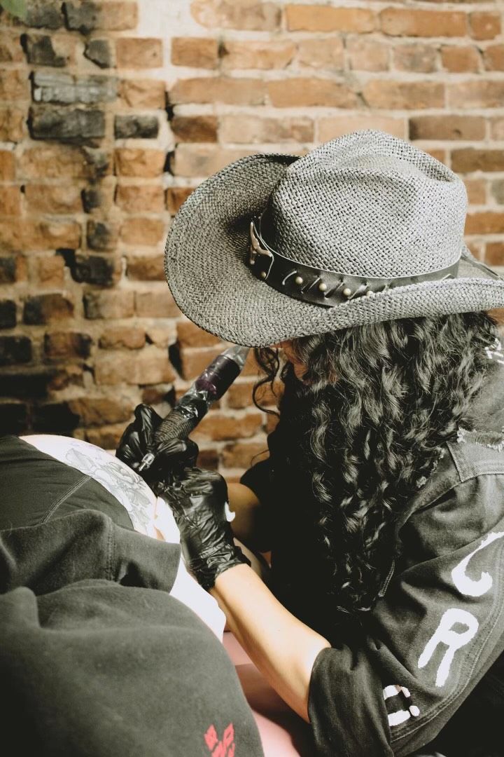 A woman wearing a cowboy hat is getting a tattoo.