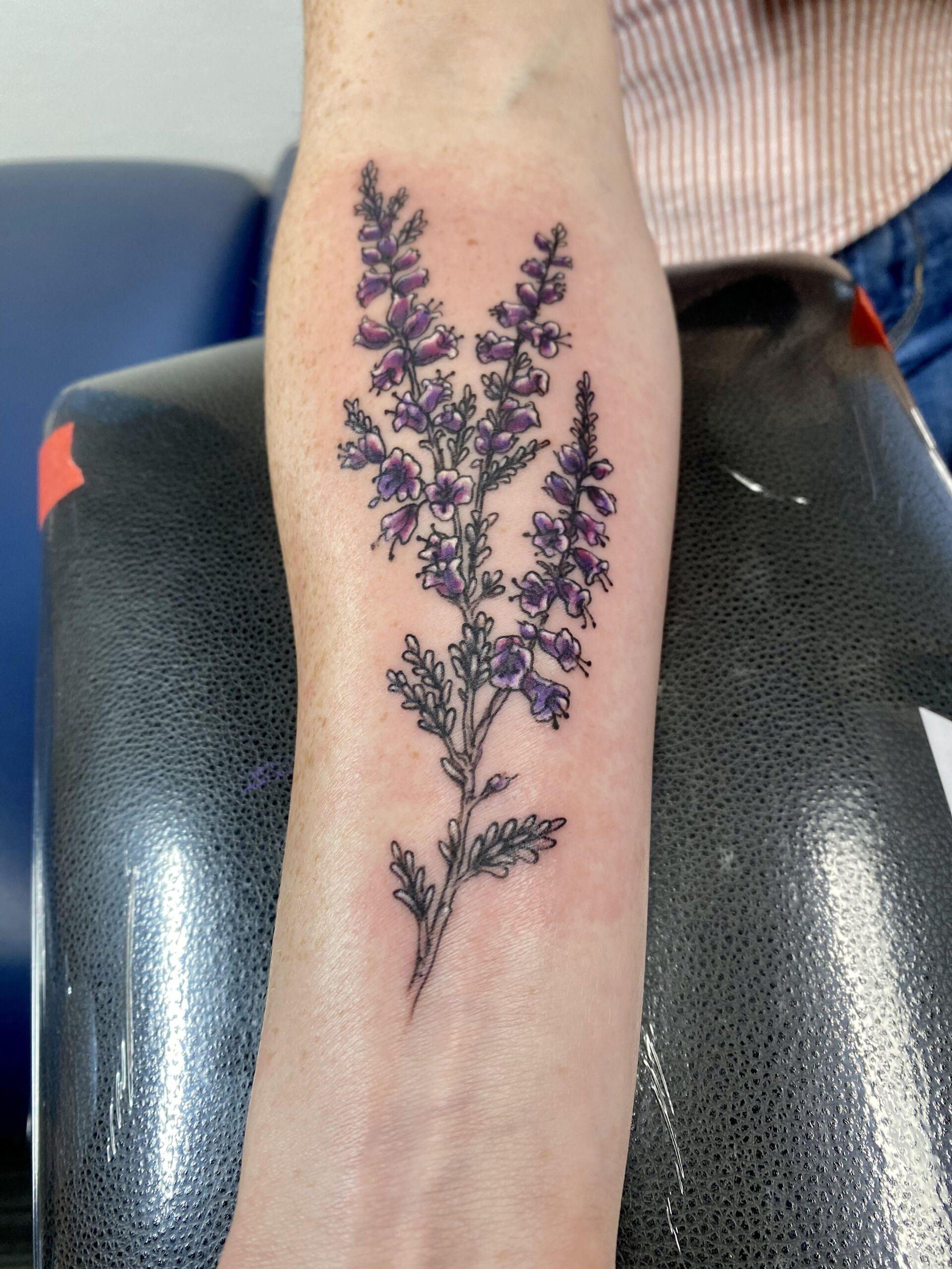 A person has a tattoo of purple flowers on their forearm