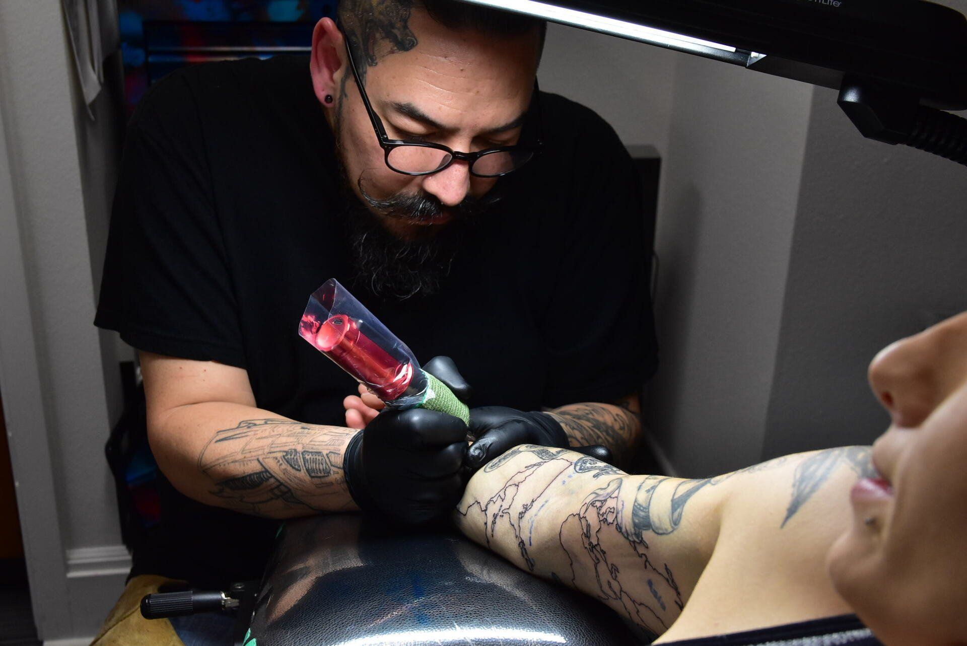 A man is getting a tattoo on a woman 's arm.