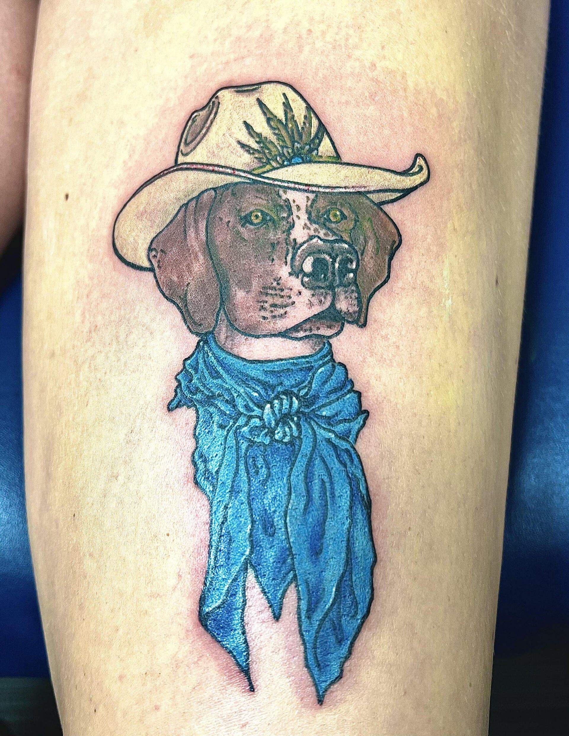 A tattoo of a dog wearing a cowboy hat and scarf