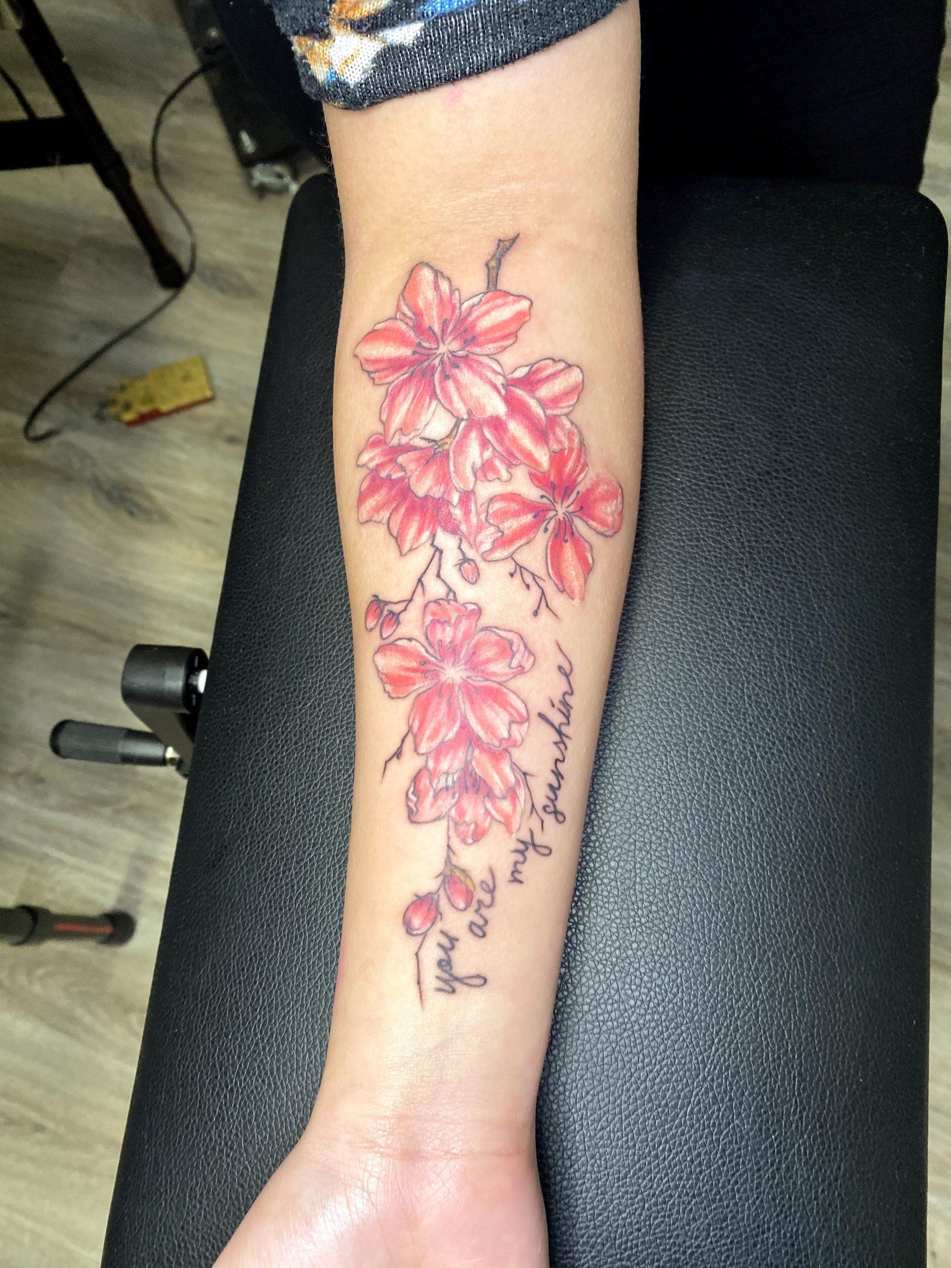 A woman has a tattoo of red flowers on her forearm