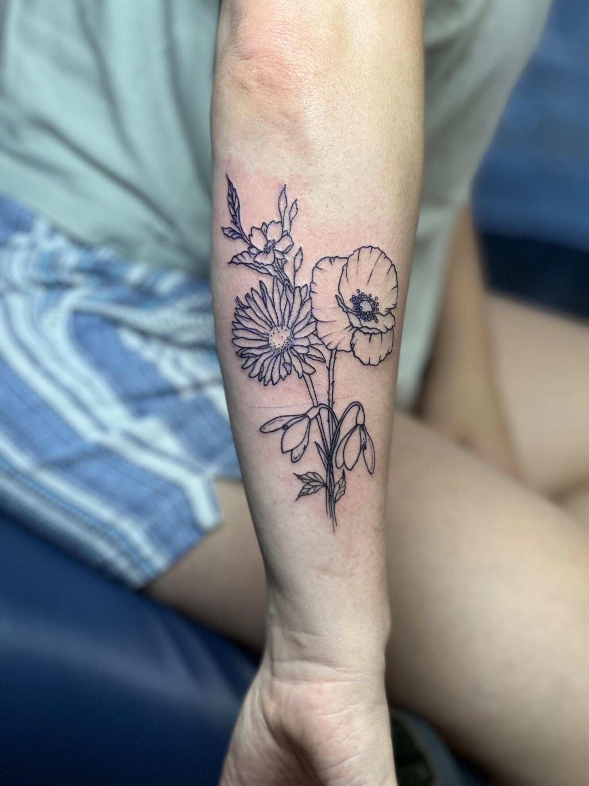 A woman has a tattoo of flowers on her forearm.