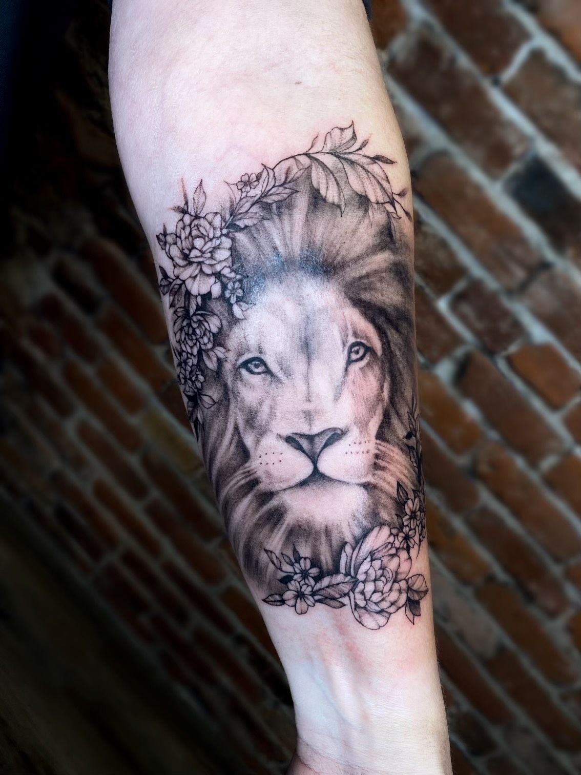 A woman has a tattoo of a lion with flowers on her forearm.