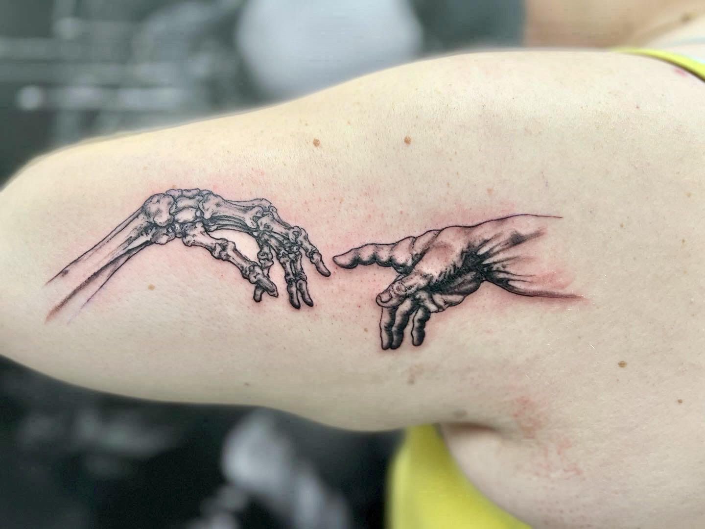 A woman has a tattoo of a skeleton hand touching another hand
