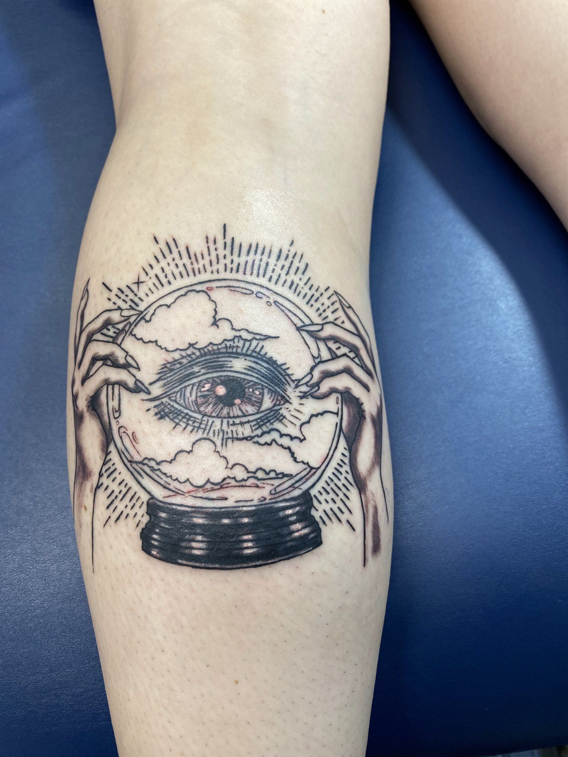 A tattoo of a person holding a crystal ball with an eye in it
