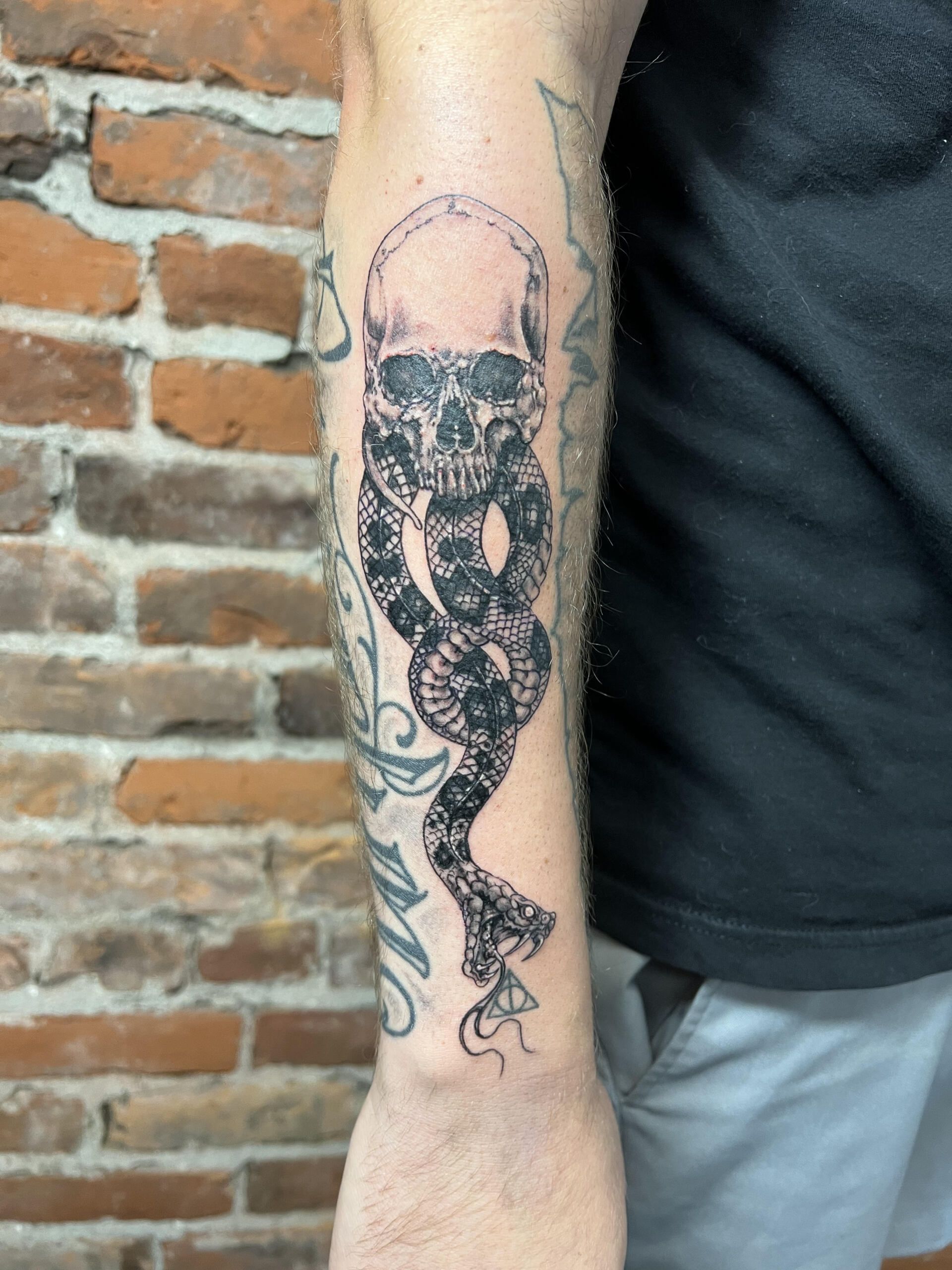 A man has a tattoo of a skull and snake on his arm