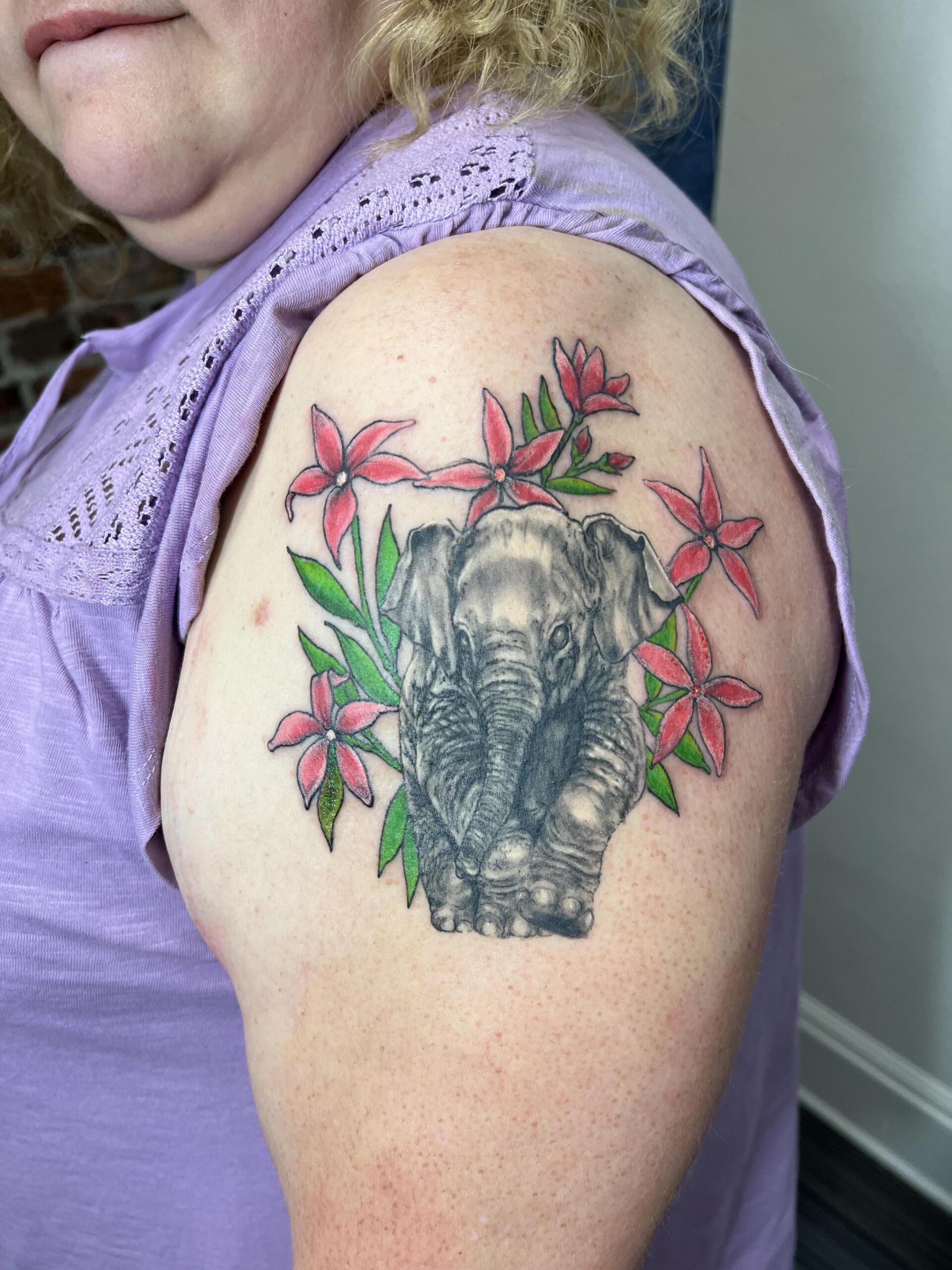 A woman has a tattoo of an elephant surrounded by pink flowers