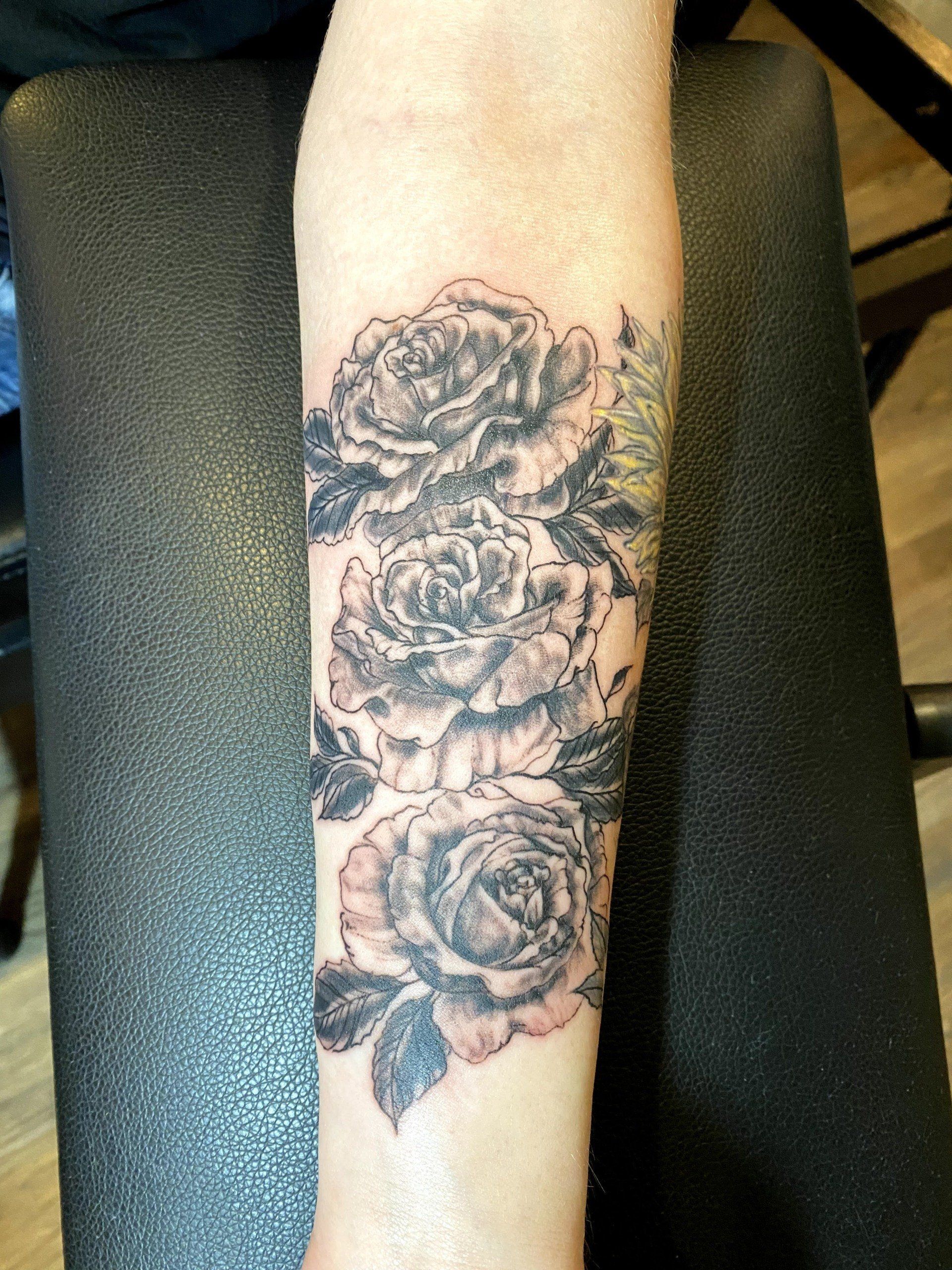 A person has a tattoo of three roses on their forearm