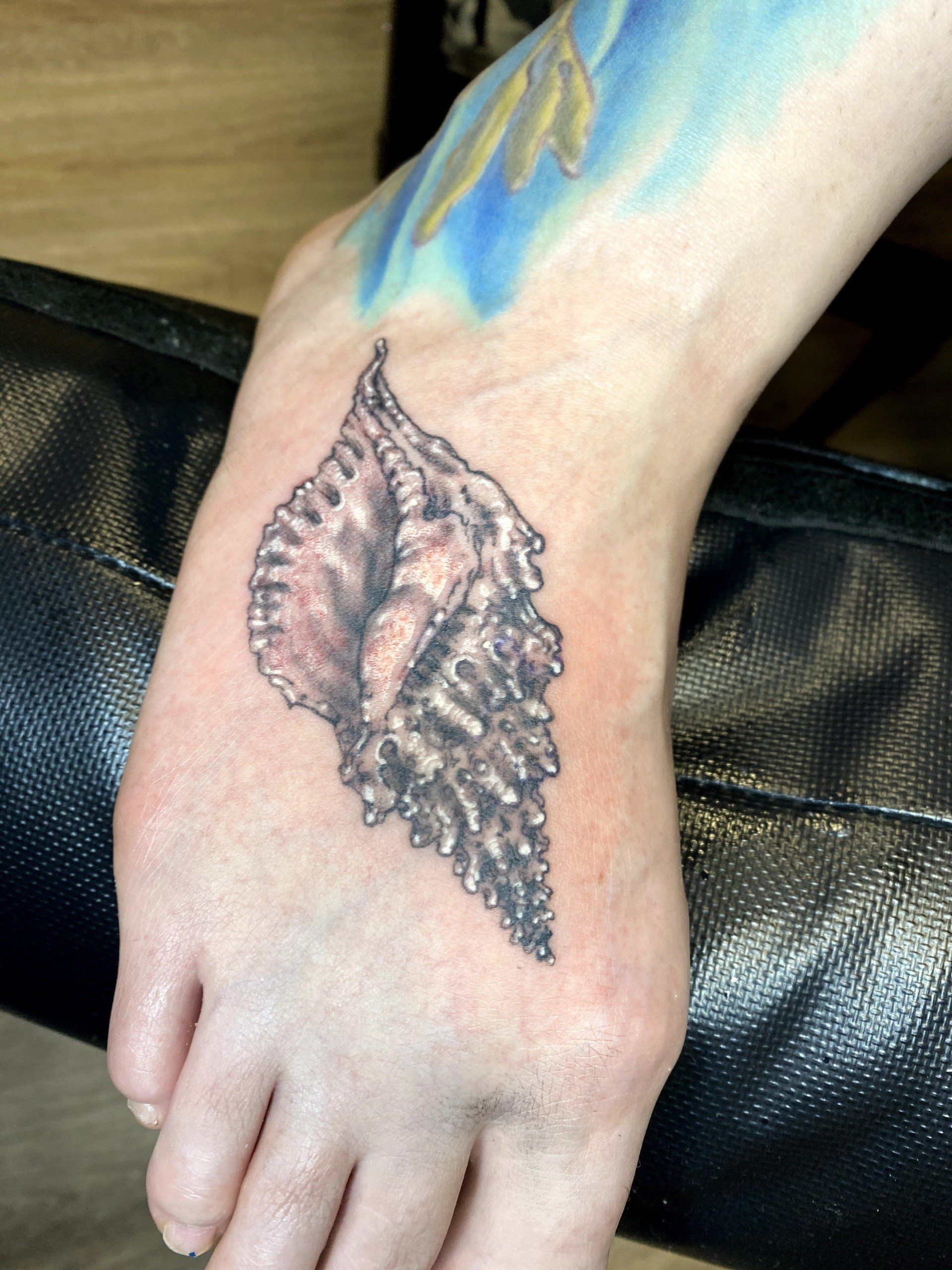 A person has a tattoo of a sea shell on their foot
