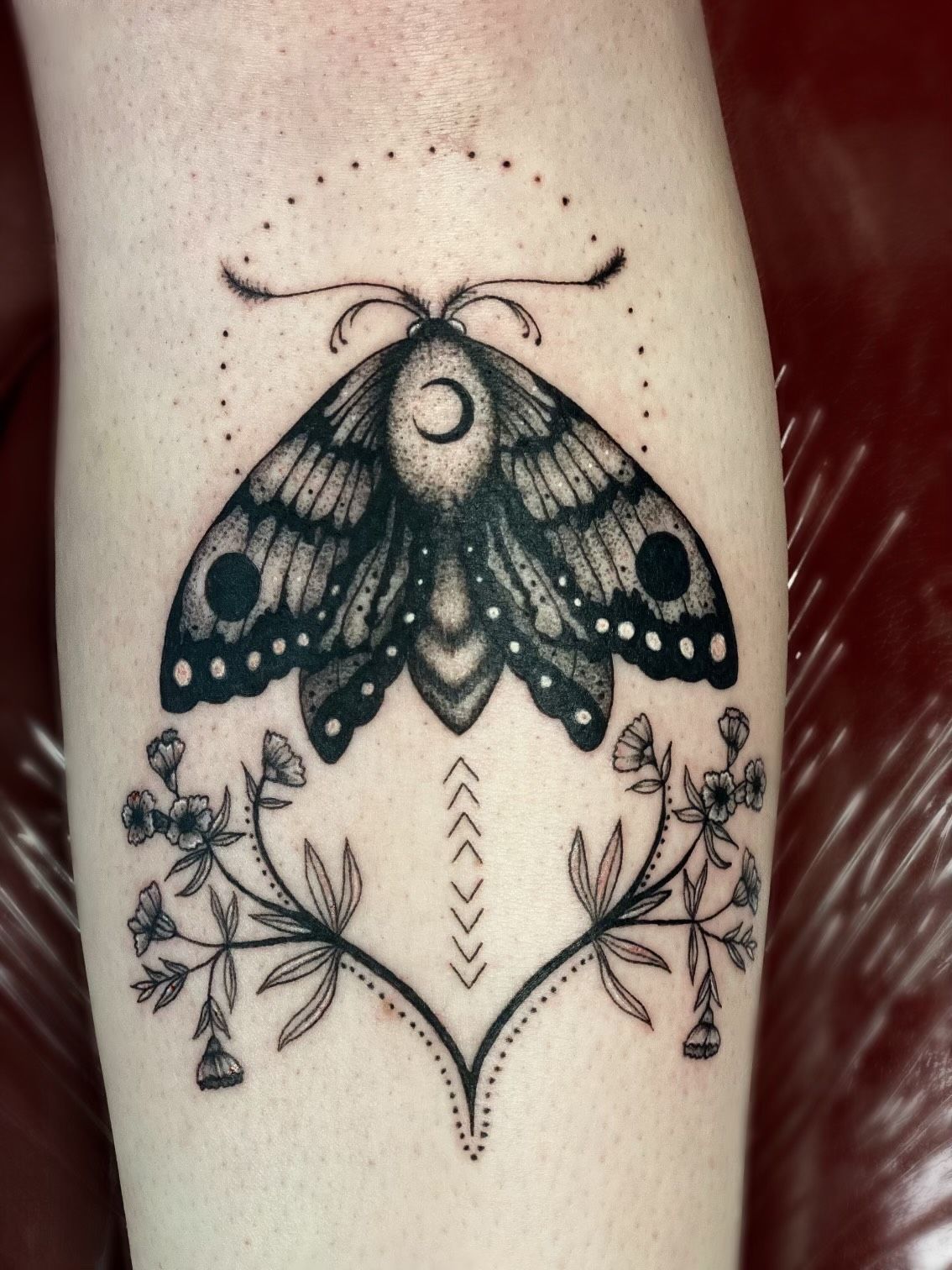 A black and white tattoo of a moth and flowers