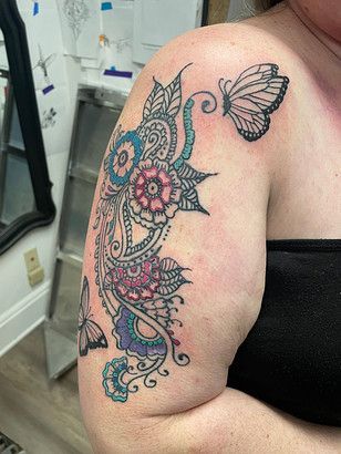 A woman has a tattoo of flowers and butterflies on her shoulder.
