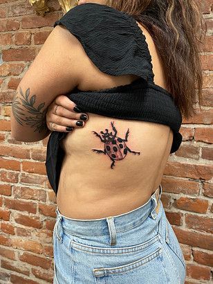 A woman has a ladybug tattoo on her side.