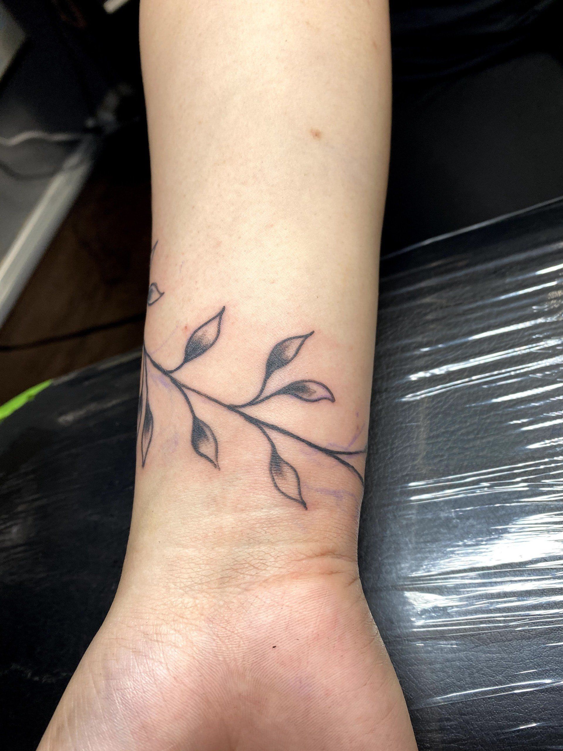 A woman has a tattoo of a branch with leaves on her wrist