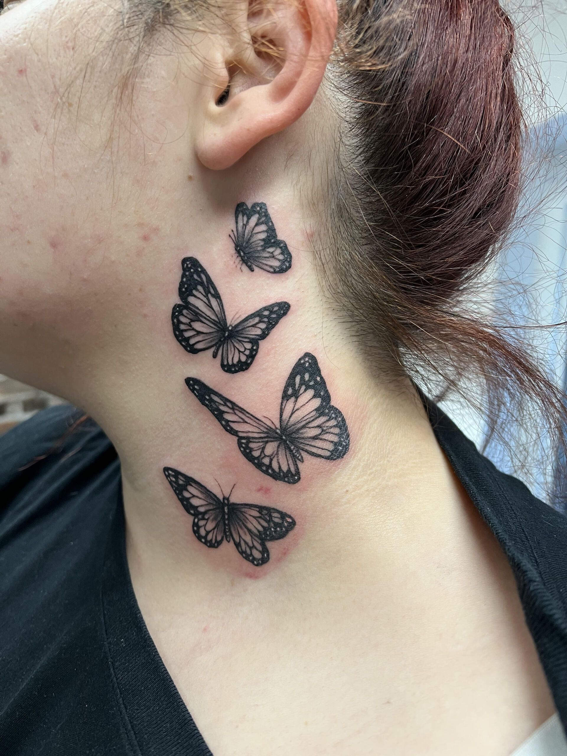 A woman has a tattoo of butterflies on her neck.