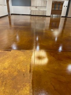 A polished concrete floor with a visible color variation between a light tan section and a glossy, dark amber section.