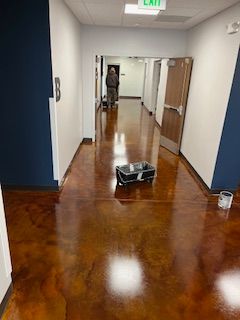 A hallway with a polished, mottled brown concrete floor, a cleaning cart, and a person walking in the distance.