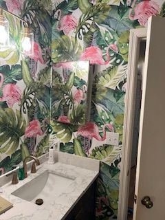 A bathroom vanity with a marble countertop, metallic faucet, and a wall covered in tropical flamingo wallpaper.