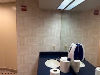 A commercial bathroom vanity with a mirror, dark blue countertop, white sink, and a paper towel dispenser.