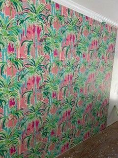 A wall covered in vibrant wallpaper featuring a repeating pattern of green palm trees and bright pink floral accents.