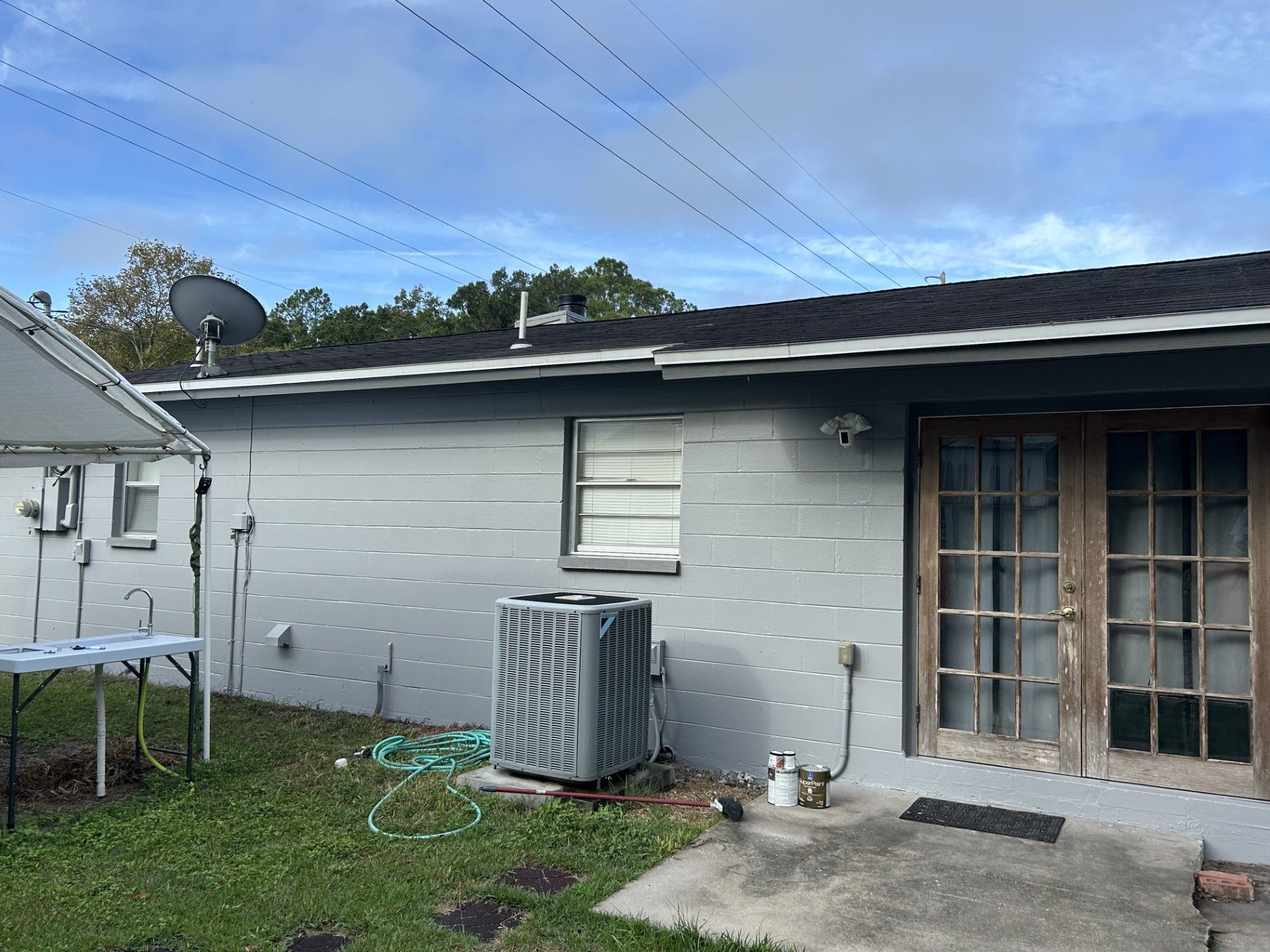 A grey exterior wall of a house with a window, a central air unit, and a set of glass pane double doors.