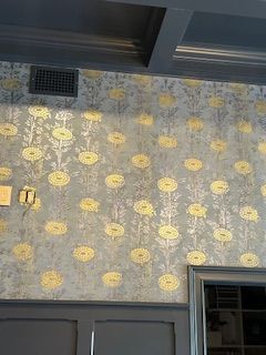 Wallpaper with gold floral patterns on a muted blue background, situated above dark gray wainscoting and trim.