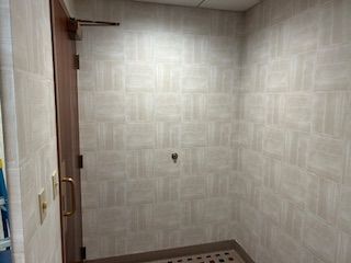 A tiled bathroom shower stall with a single metal hook on the back wall and a partially visible door on the left.