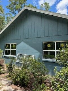 A blue house exterior with a gable roof, two windows with yellow stickers, and a spare window leaning against the wall.