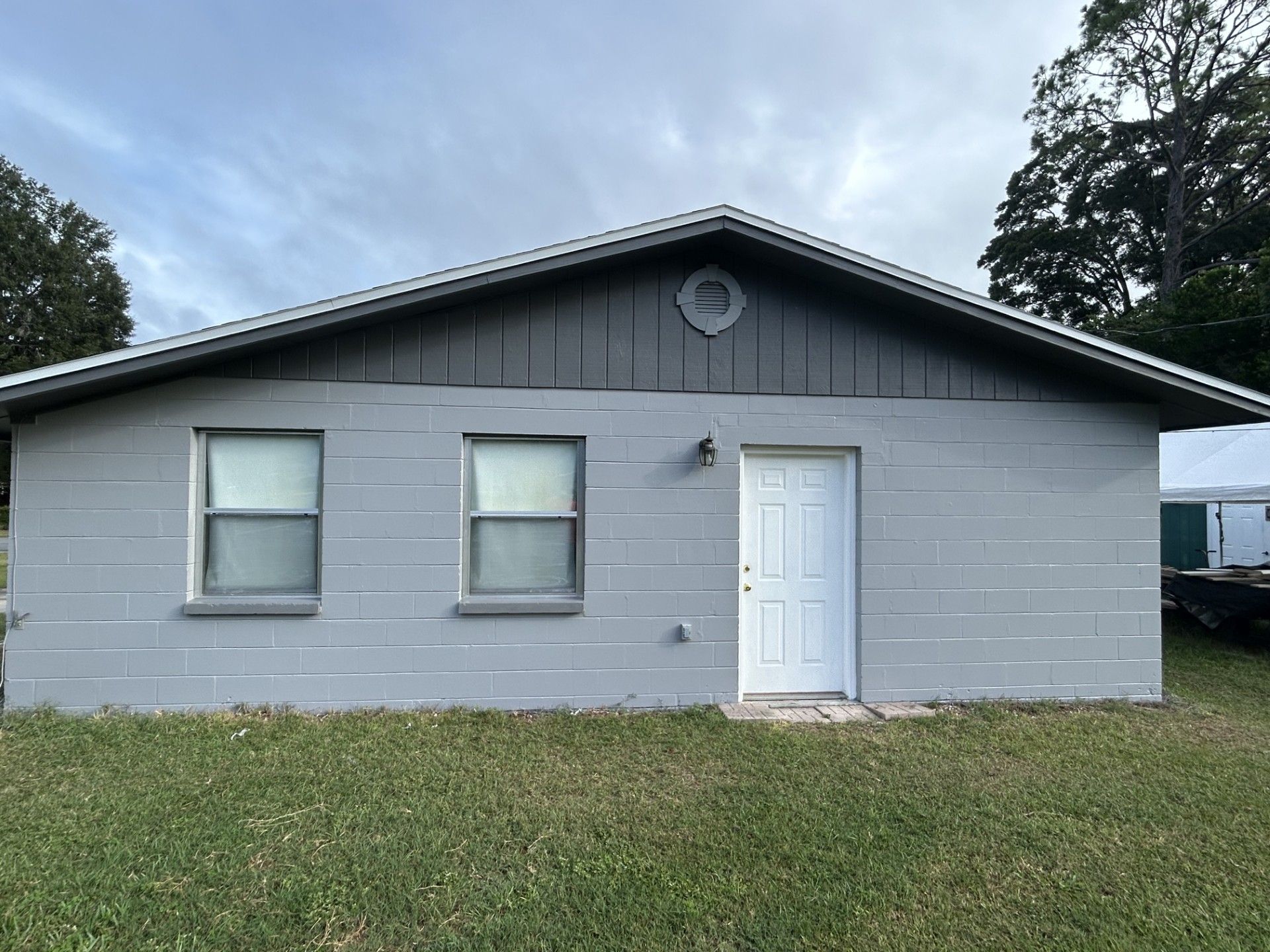 A gray, single-story house with two windows and a white front door under a gray gabled roof on a grassy lawn.
