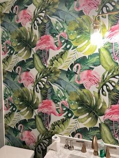 A bathroom wall covered in tropical wallpaper featuring pink flamingos and green monstera leaves above a vanity.