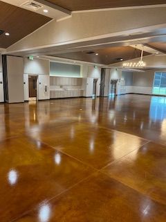 A spacious event hall with polished brown concrete floors, neutral walls, recessed lighting, and a chandelier.