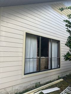 Light-colored siding on a home's exterior wall with a window featuring dark trim and white curtains.