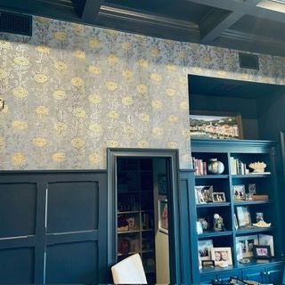 A room with dark blue wainscoting and cupboards featuring floral wallpaper above, with a built-in bookshelf on the right.