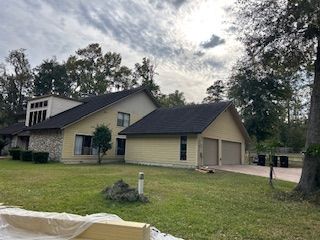 A yellow house with a two-car garage, stone accents, and a dark roof under a cloudy sky.