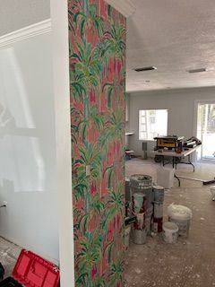 A vertical column covered in vibrant pink and green floral wallpaper stands in a room undergoing interior renovation.