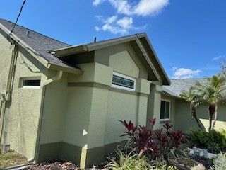 Exterior view of a light green house with a dark green base, dark gray shingled roof, and a small rectangular window.